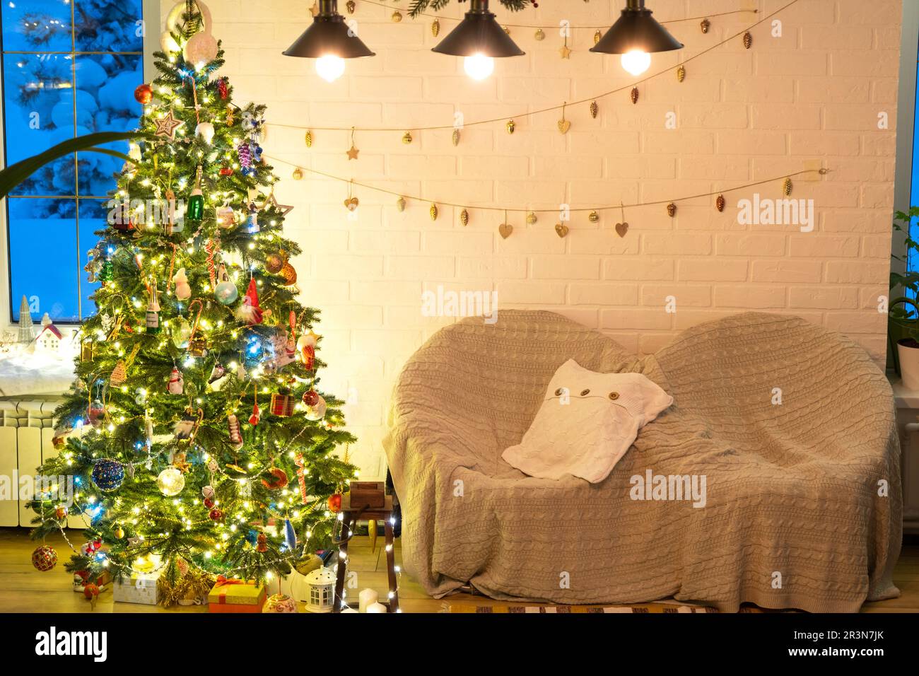 Arbre de Noël dans l'intérieur blanc d'une maison avec des murs de briques de style loft avec guirlande de jouets en verre sur une corde. Lig de fées lumineux Banque D'Images