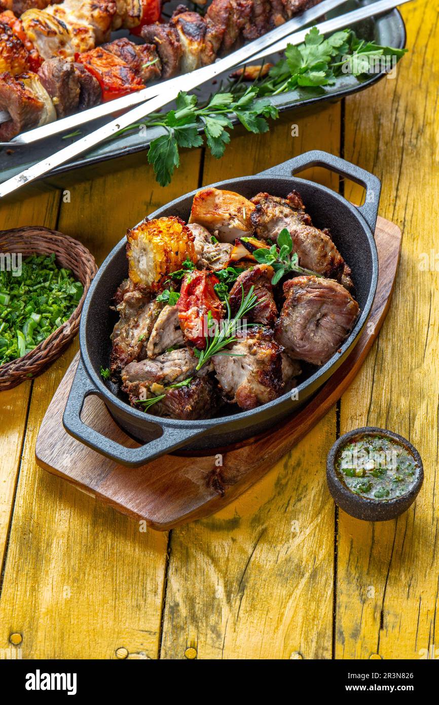 Viande grillée au barbecue - porc, poulet et légumes sur une poêle en fonte. Brochettes grillées sur fond de bois jaune. Vue de dessus Banque D'Images