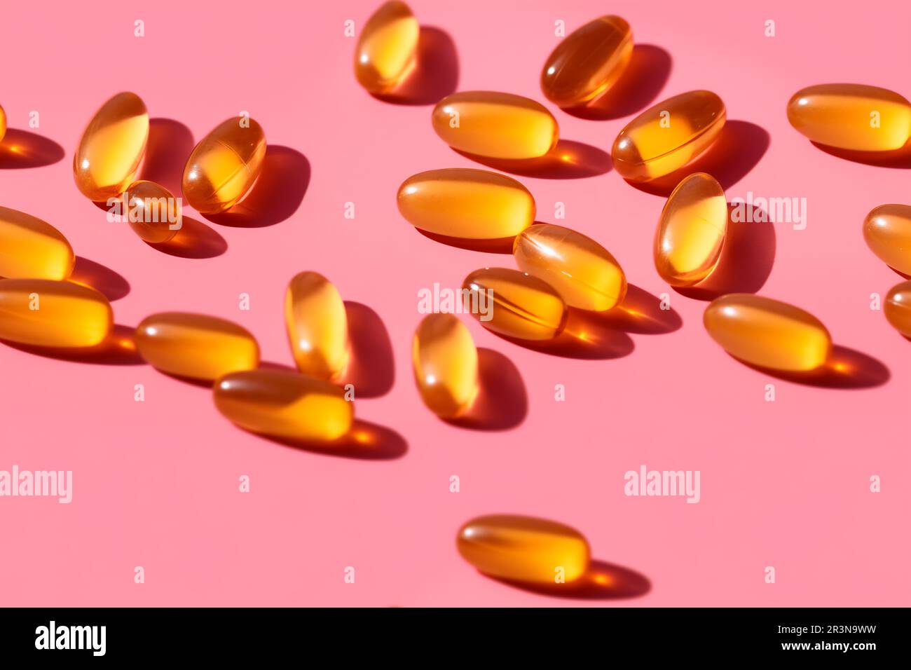 Composition de pilules de vitamine orange dispersées sur fond rose en studio léger Banque D'Images