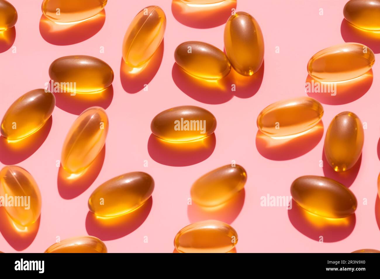 Composition de pilules de vitamine orange dispersées sur fond rose en studio léger Banque D'Images