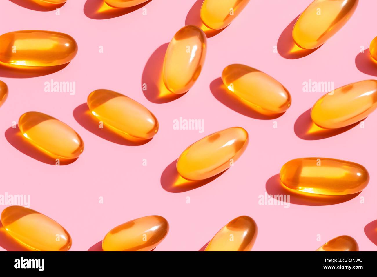 Composition de pilules de vitamine orange dispersées sur fond rose en studio léger Banque D'Images
