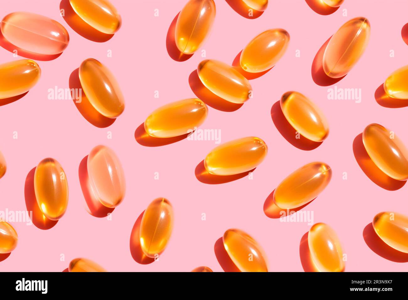 Composition de pilules de vitamine orange dispersées sur fond rose en studio léger Banque D'Images