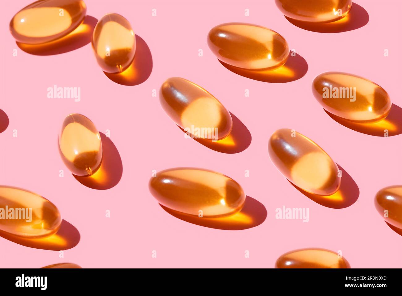 Composition de pilules de vitamine orange dispersées sur fond rose en studio léger Banque D'Images