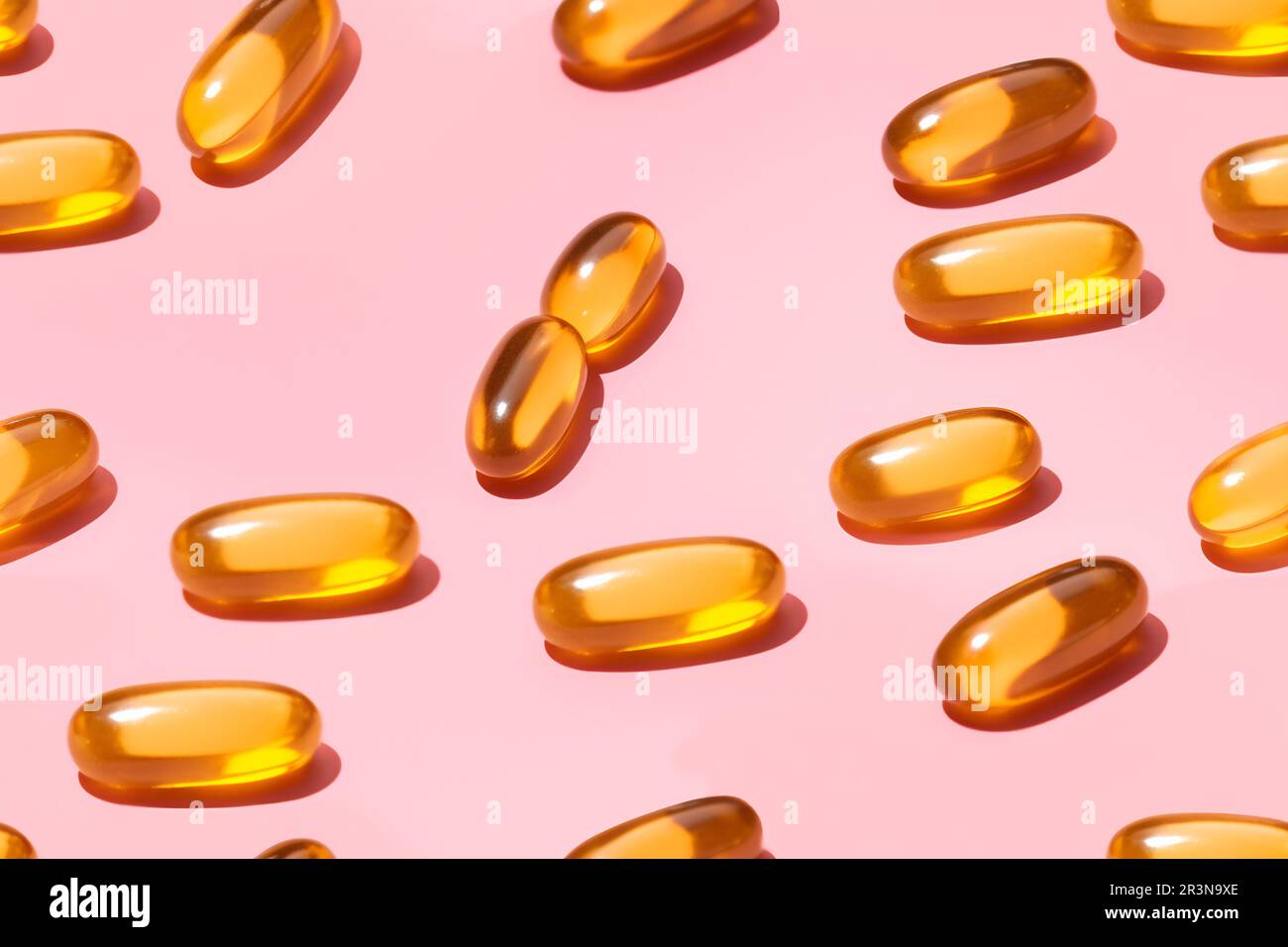 Composition de pilules de vitamine orange dispersées sur fond rose en studio léger Banque D'Images