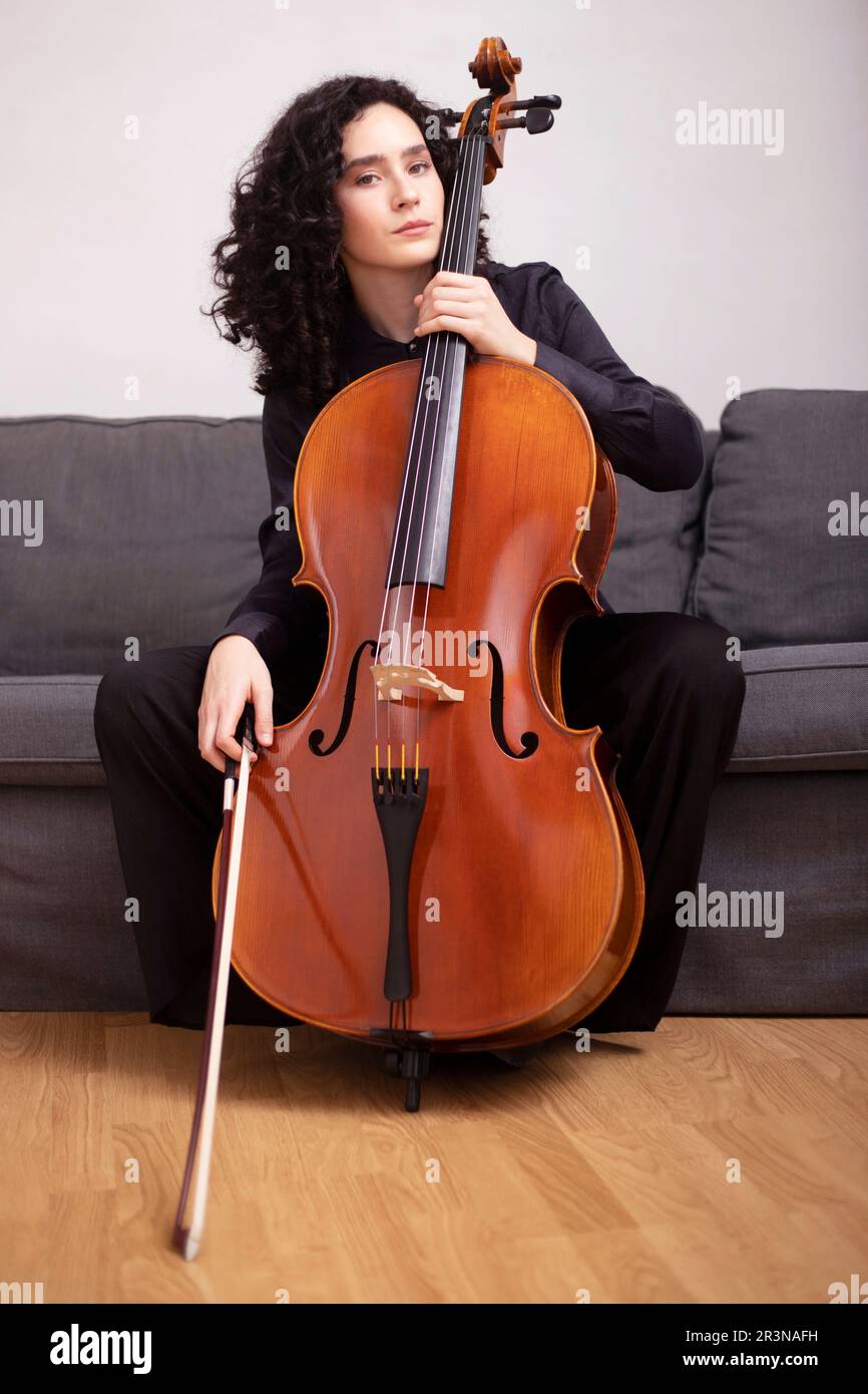 Calme femme musicienne dans des vêtements noirs formels assis sur un canapé  et jouer de violoncelle acoustique avec le violoncelle de violon tout en  regardant l'appareil photo Photo Stock - Alamy