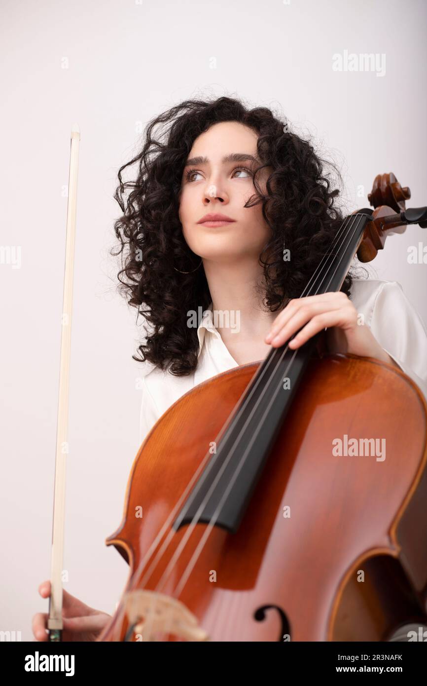 Calme femme musicienne dans des vêtements blancs formels assis jouant du violoncelle  acoustique avec le violoncelle de violon tout en regardant loin Photo Stock  - Alamy
