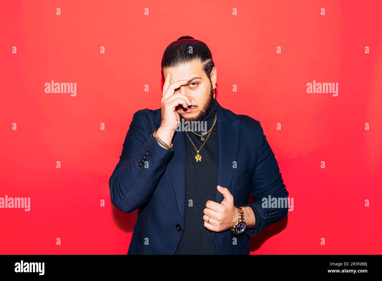 Portrait d'un jeune homme sérieux en costume tendance avec montre-bracelet et accessoires coûteux regardant l'appareil photo avec la main sur le visage tout en se tenant contre r Banque D'Images