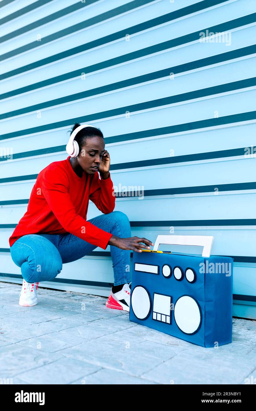 Ensemble complet de femmes afro-américaines dans des écouteurs écoutant la liste de lecture de chansons funky tout en étant assis près de la boombox sur le trottoir Banque D'Images