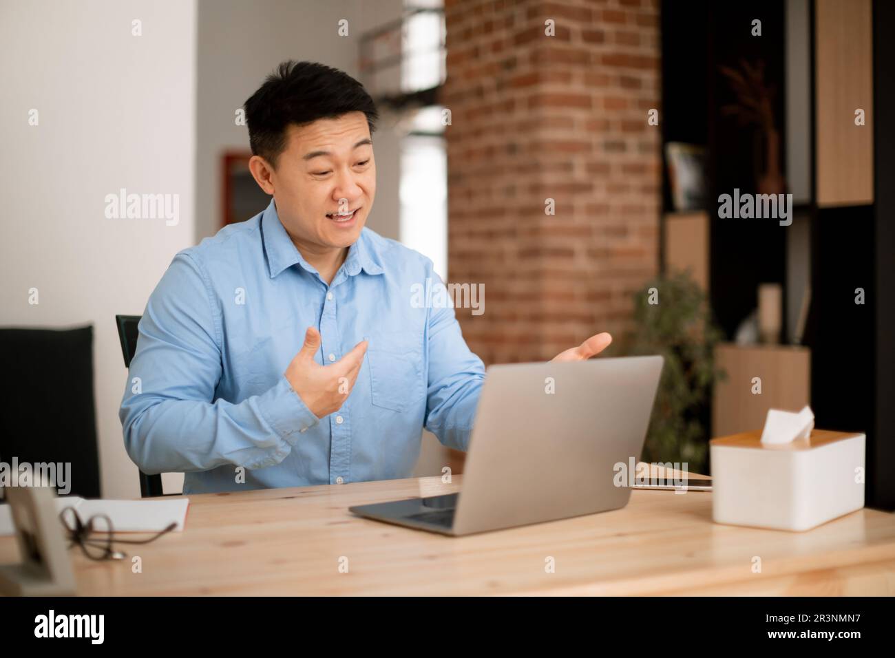 Homme asiatique joyeux d'âge moyen utilisant un ordinateur portable, ayant des appels vidéo avec des collègues de la maison tout en travaillant à distance Banque D'Images