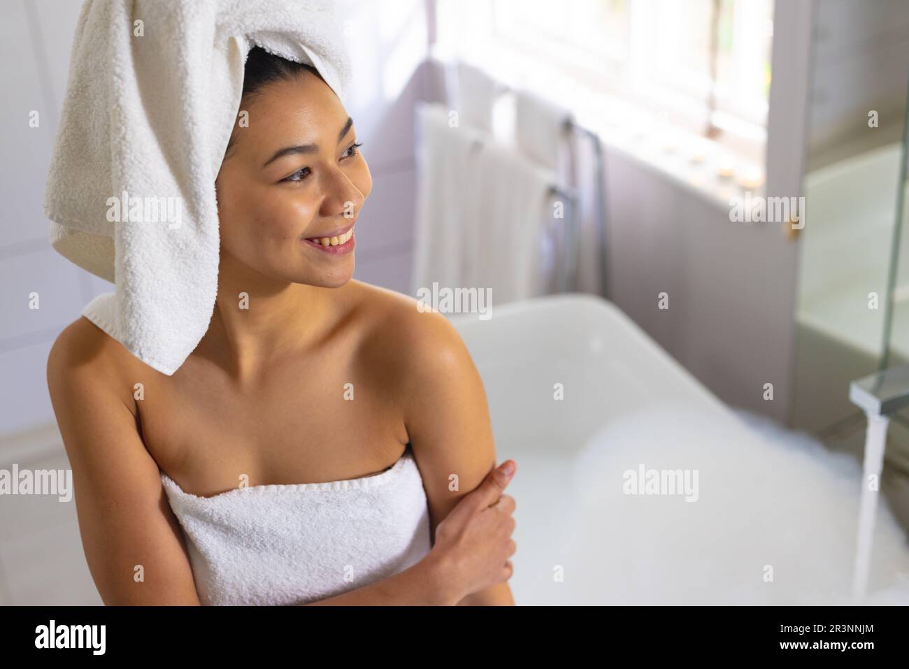Bonne femme biraciale portant une serviette de bain dans la salle de bains,  avec un espace copie. Détente, soin de soi, beauté, loisirs et concept de  style de vie Photo Stock -