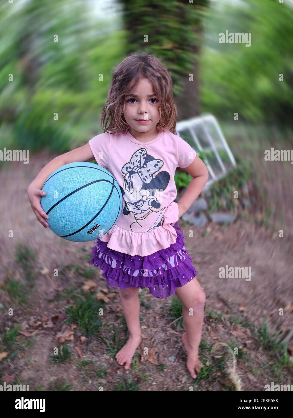 Fille posant avec un basket dehors. Elle a une expression décontractée, tandis que la toile de fond a un effet de rotation Banque D'Images