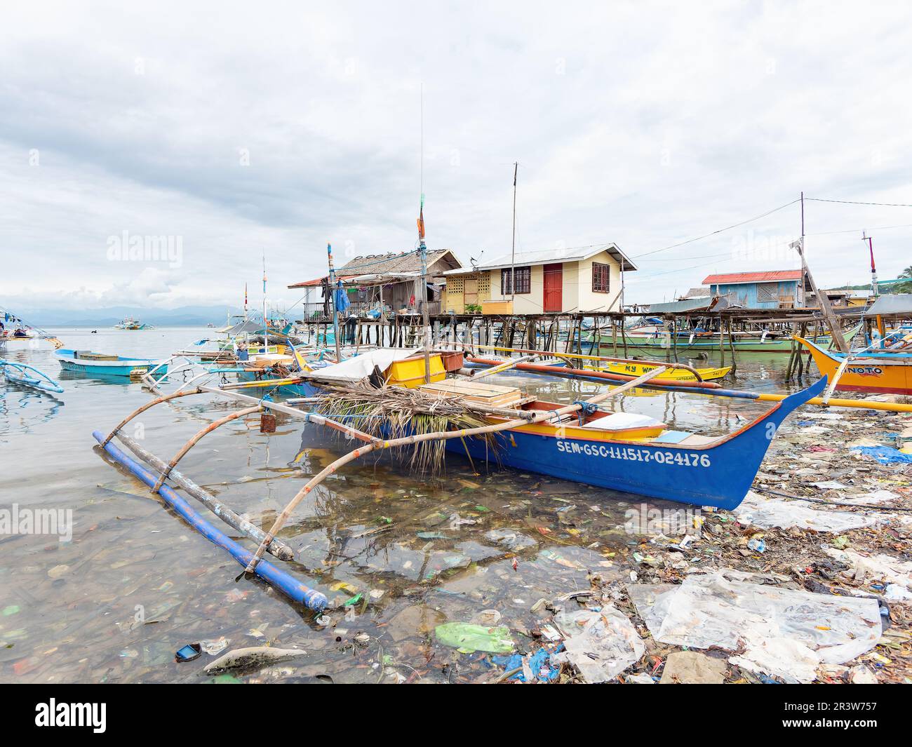 Sarangani, Philippines - 17 janvier 2018: Un bateau de pêche traditionnel en outrigger flottant dans une mer de la malbouffe à ce qui était autrefois une plage vierge dans le v Banque D'Images