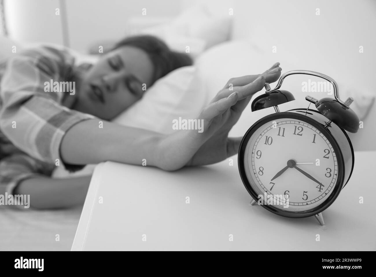 Jeune femme endormie qui éteint le réveil à la maison le matin, foyer sélectif. Photographie en noir et blanc Banque D'Images
