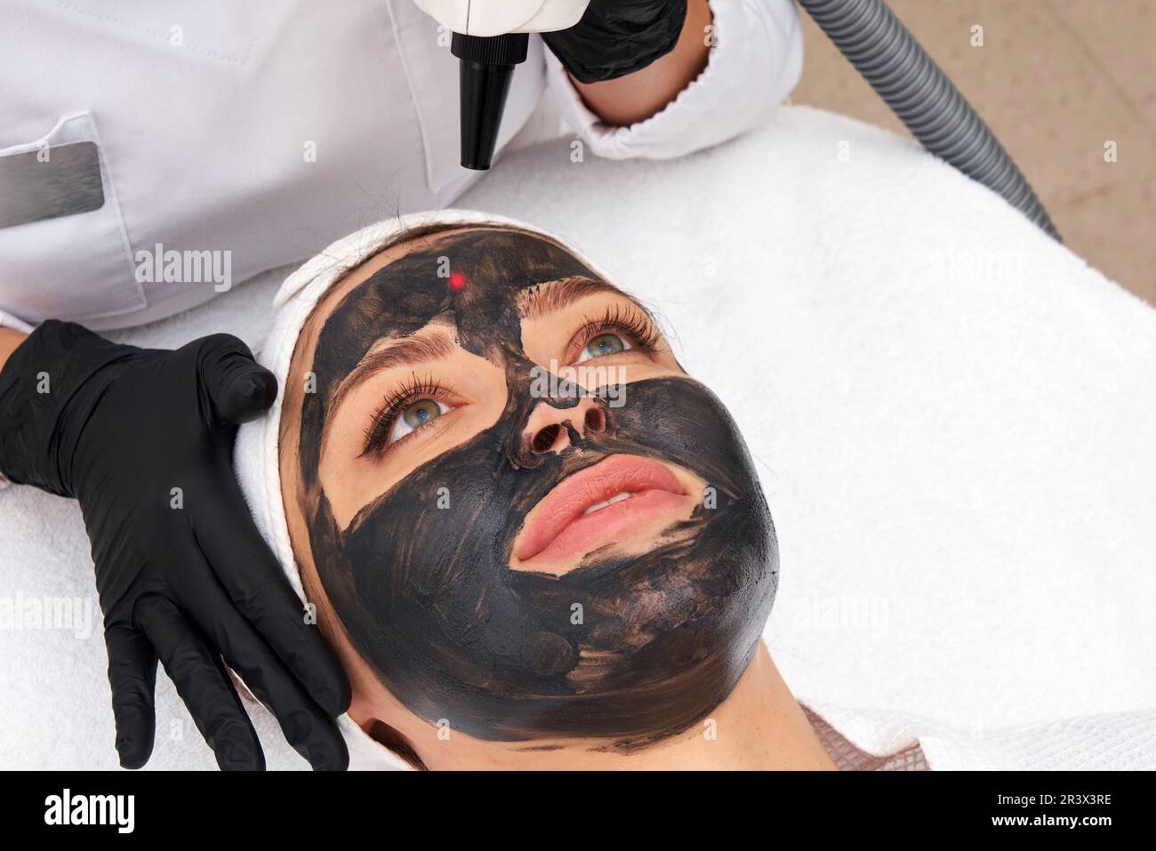 Cosmétologue appliquant un masque noir sur le visage d'une belle femme pour le pelage du carbone Banque D'Images