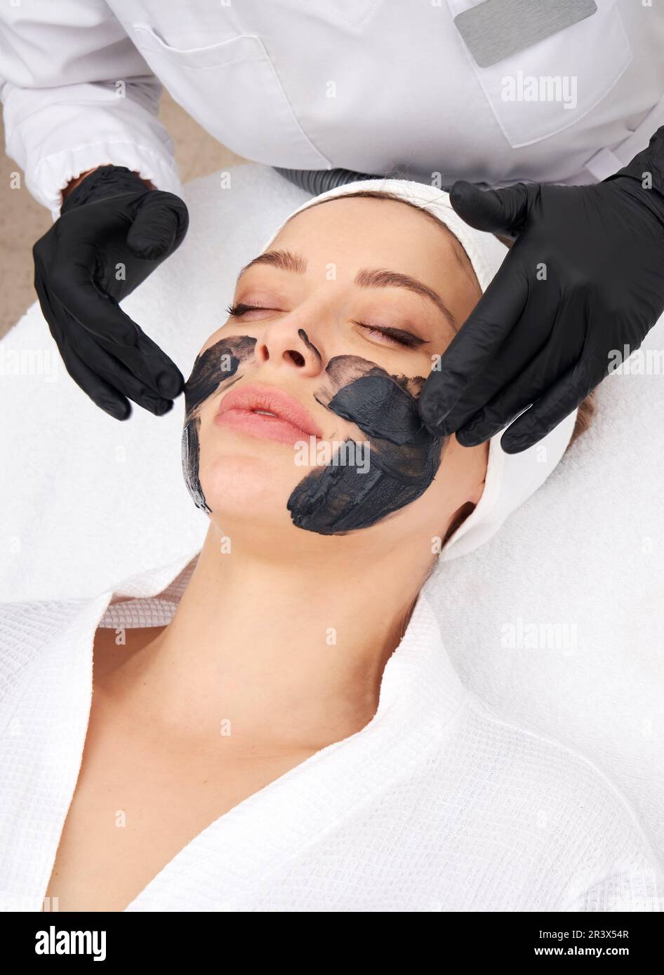 Cosmétologue appliquant un masque noir sur le visage d'une belle femme pour le pelage du carbone Banque D'Images