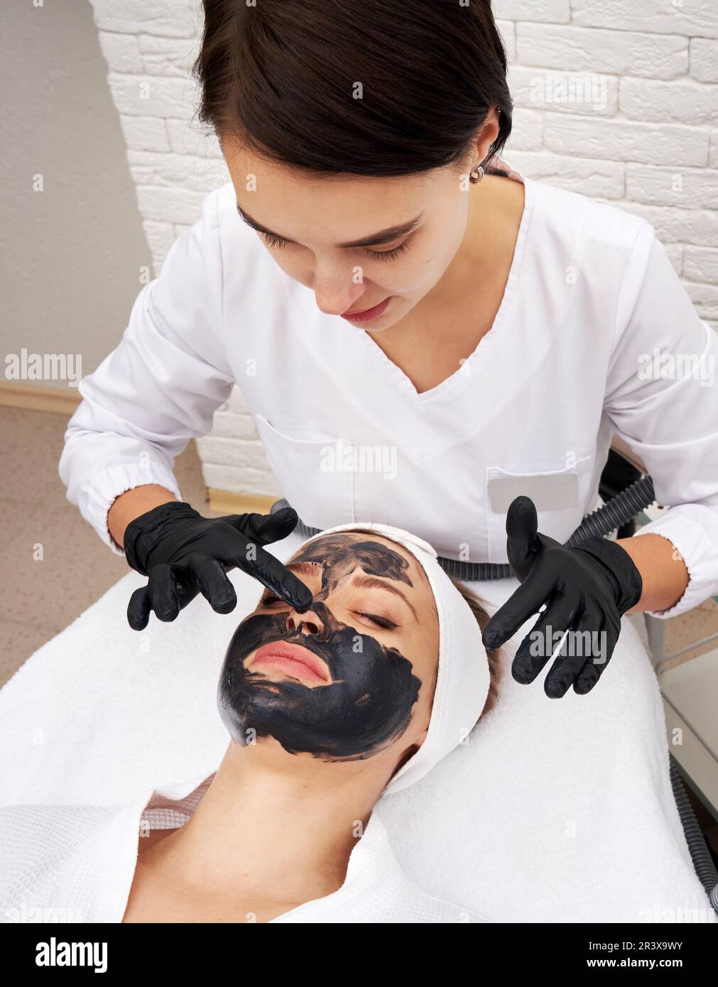 Cosmétologue appliquant un masque noir sur le visage d'une belle femme pour le pelage du carbone Banque D'Images