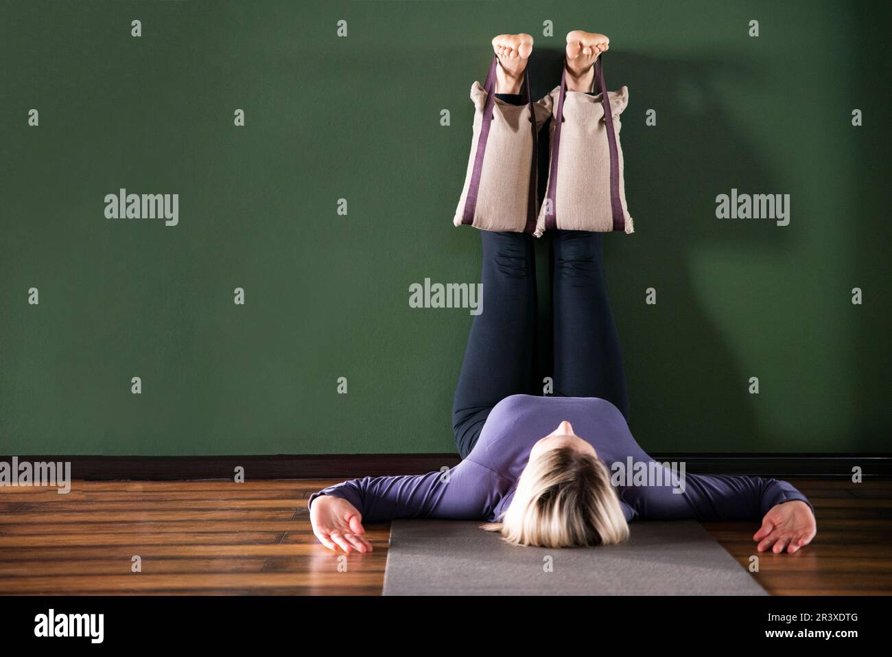 Jeune femme en yoga relaxant poser avec les jambes contre le mur avec de lourds sacs de sable Banque D'Images