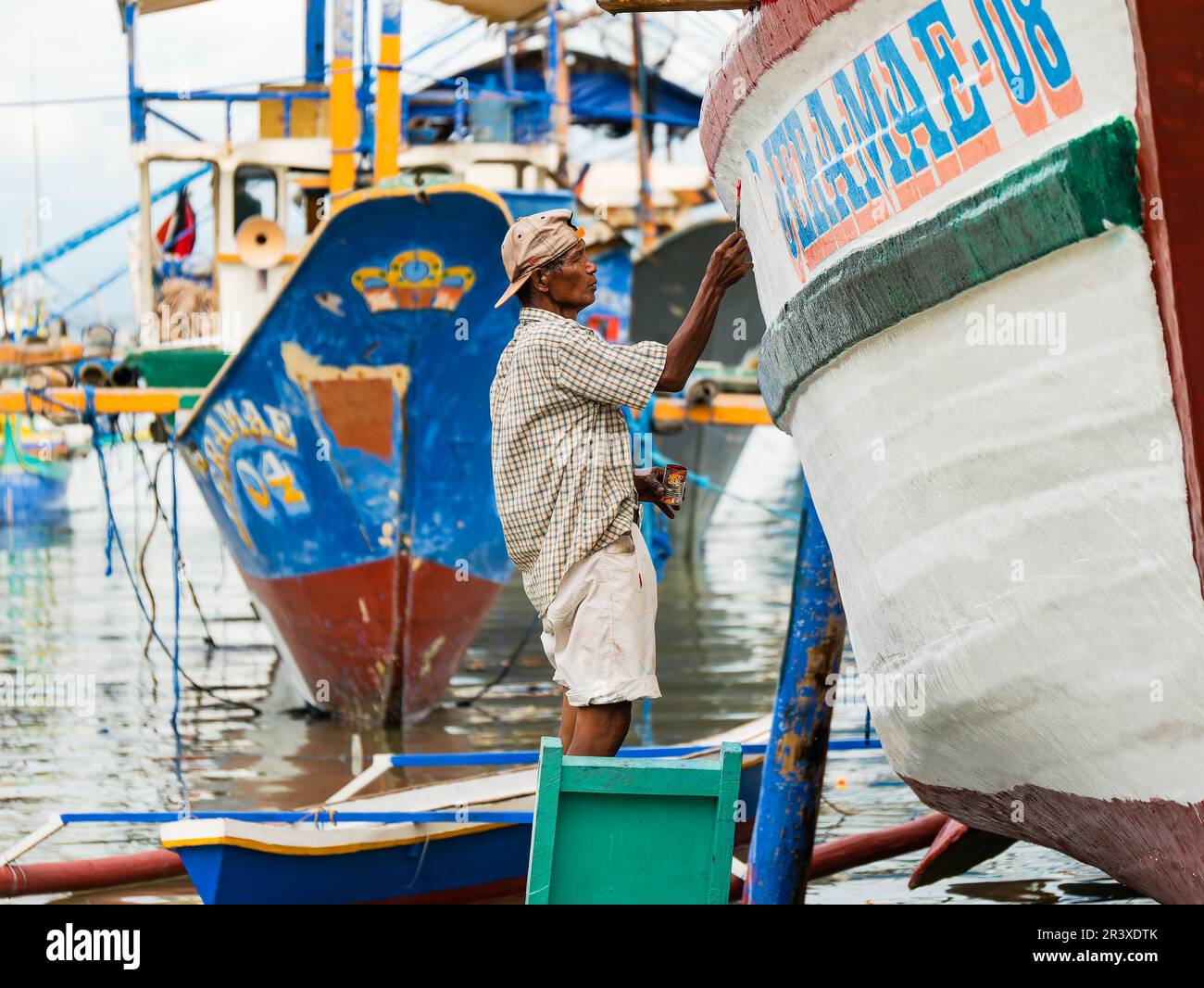 Homme effectuant des travaux de peinture sur un bateau de pêche au chantier naval de base sur la plage de Tinoto, Maasim, situé dans la province de Sarangani aux Philippines. Banque D'Images