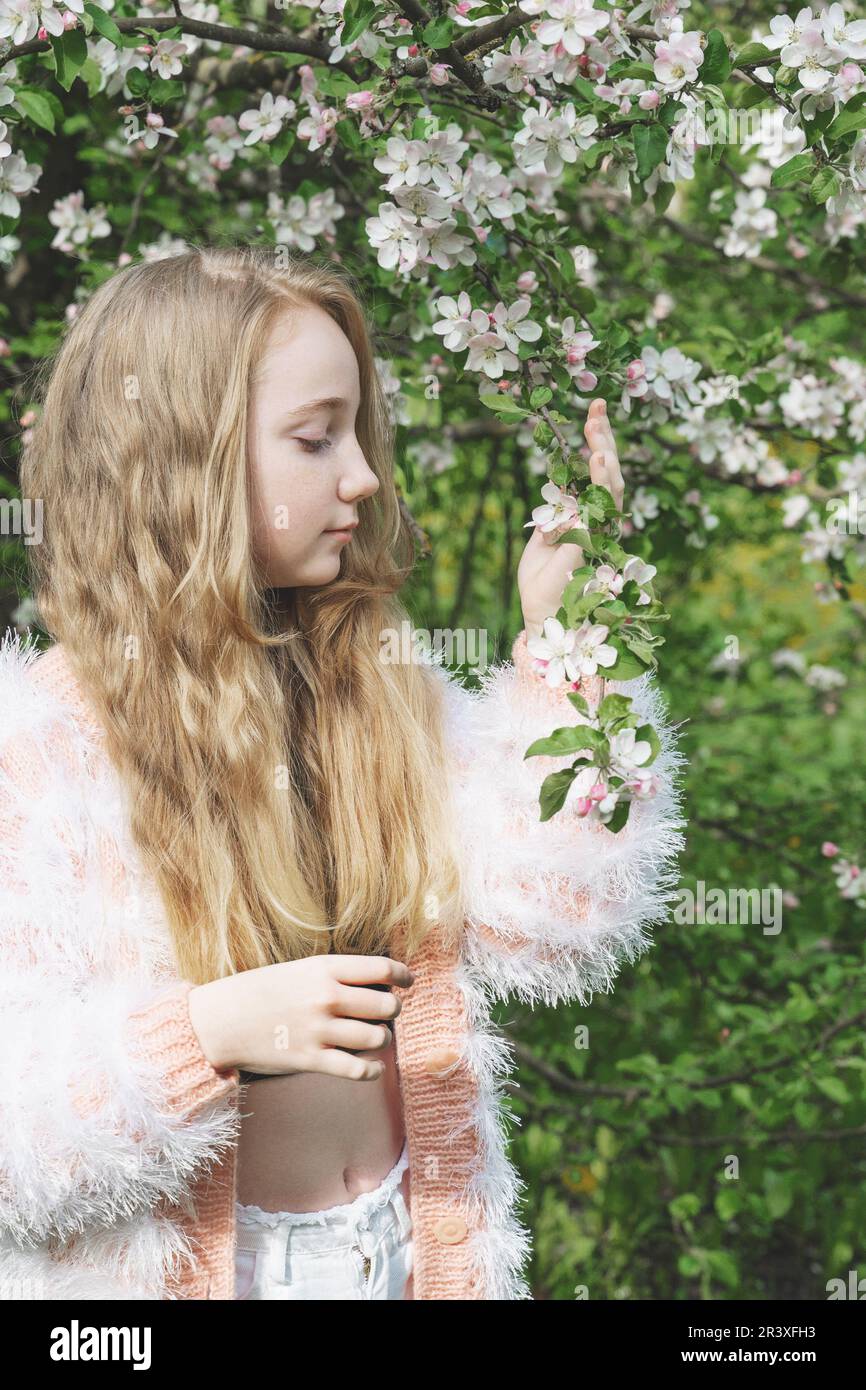 une belle fille de 13-15 ans sourit dans le jardin de printemps, luttant avec la dépression de printemps et appréciant les fleurs. Une fille heureuse est souriante dans na Banque D'Images