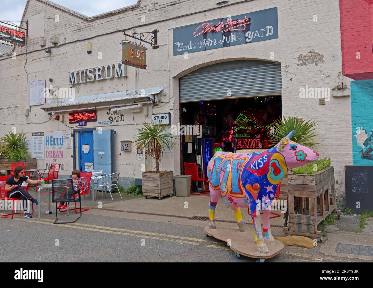 Extérieur de God’s Own Junkyard à Walthamstow, East London, montrant l’entrée du lieu d’art au néon et une sculpture de vache peinte aux couleurs vives à l’extérieur Banque D'Images