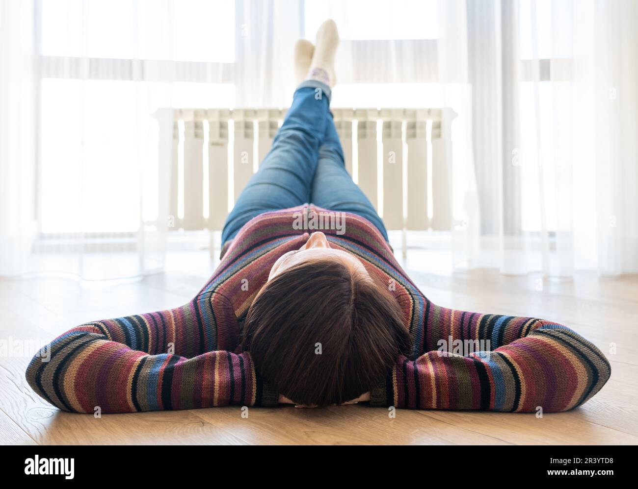 Femme posée sur le sol avec les pieds relevés sur le radiateur pour se réchauffer Banque D'Images