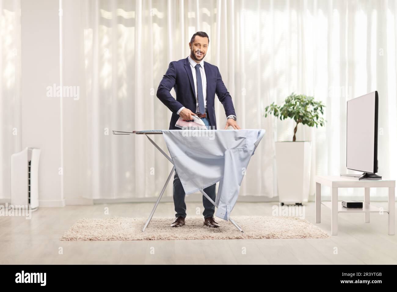 Homme d'affaires repassant une chemise à la maison devant la télévision Banque D'Images