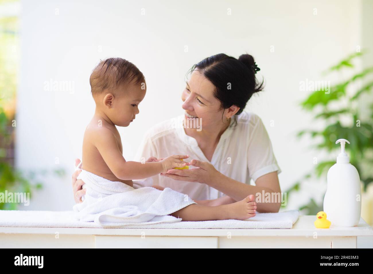 Mère changeant de couche sur bébé nouveau-né. Maman et bébé garçon riant après le bain ou la douche. Soins de la peau pour les jeunes enfants. Femme asiatique changeant de couche. Bain Banque D'Images