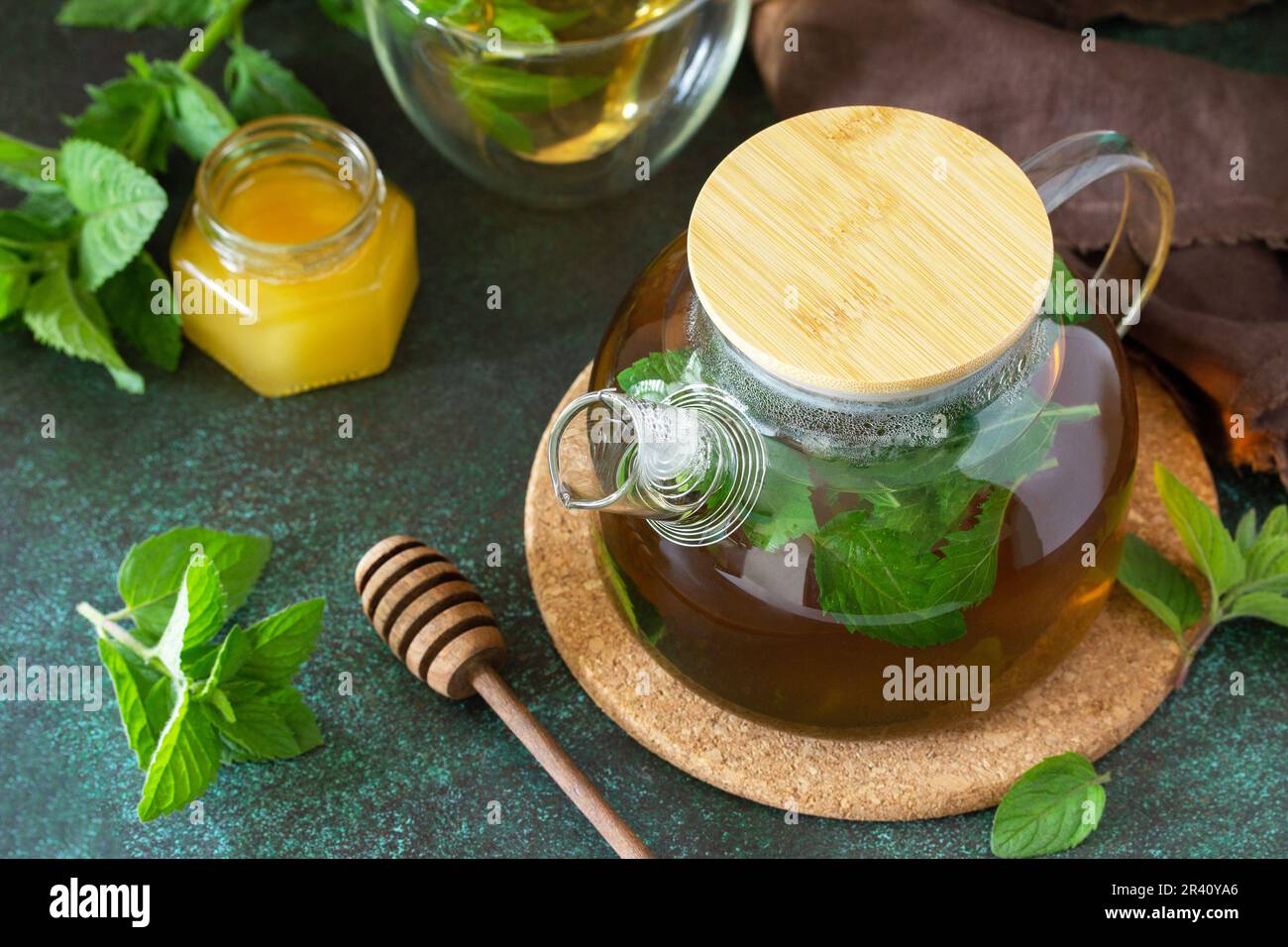 Thé vert à base de plantes thérapeutiques. Thé chaud avec des minthes de miel dans une théière en verre sur une table en pierre. Banque D'Images