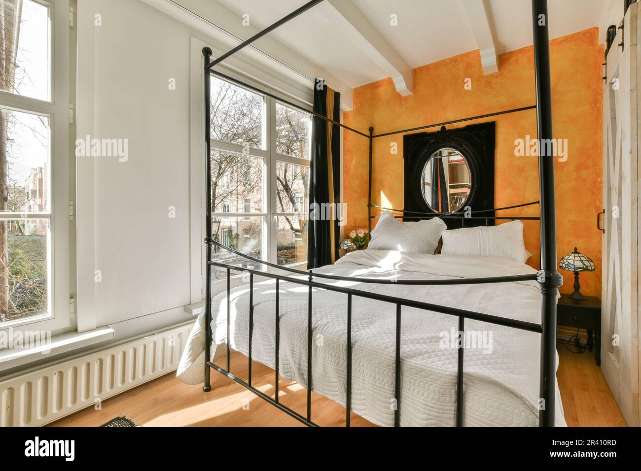 un lit dans une chambre avec des murs orange et des draps blancs sur le lit, cadre en métal noir autour de la tête de lit Banque D'Images
