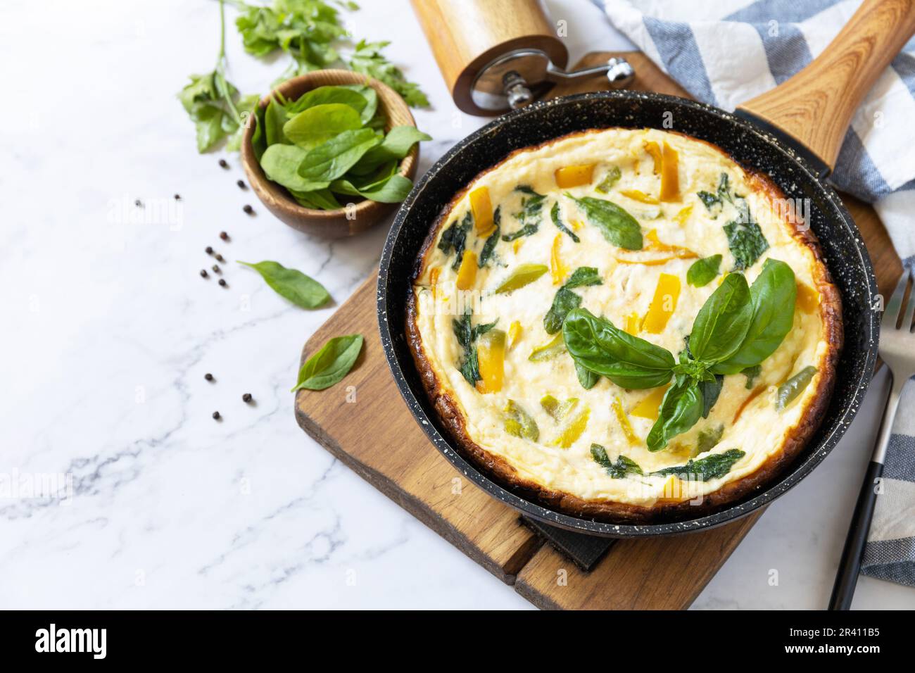 Omelette aux épinards et au fromage. Frittata fait d'oeufs, de paprika et d'épinards dans une poêle sur un comptoir en marbre. Copier l'espace. Banque D'Images