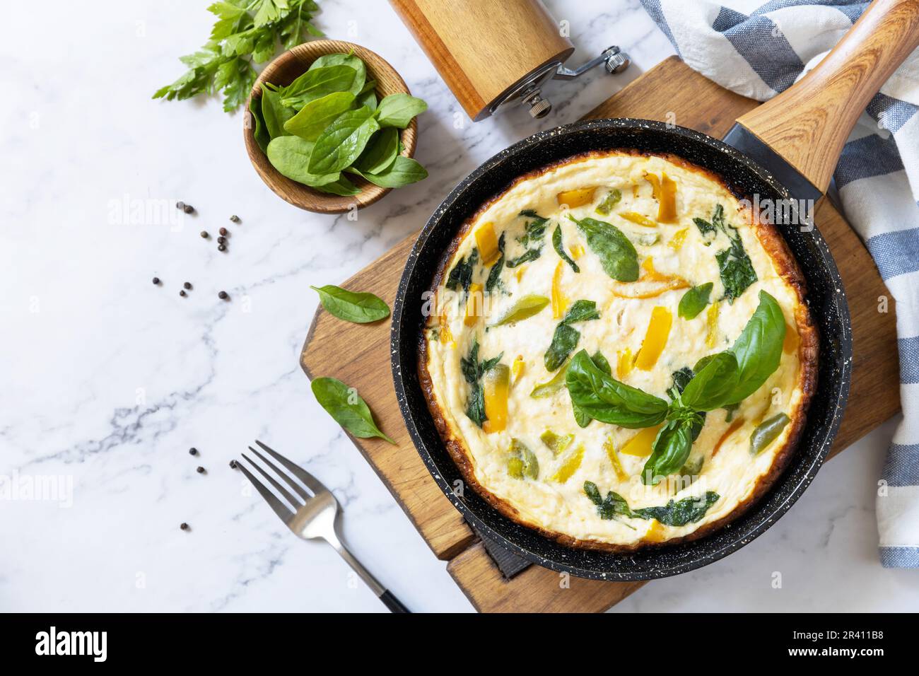 Omelette aux épinards et au fromage. Frittata fait d'oeufs, de paprika et d'épinards dans une poêle sur un comptoir en marbre. Vue de dessus. Banque D'Images