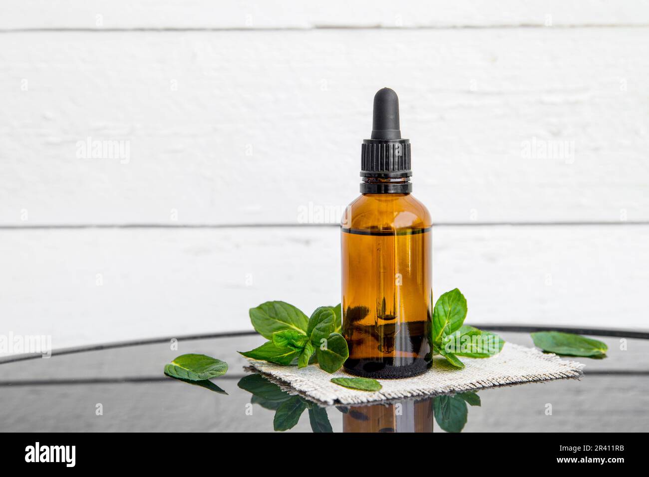 Bouteille brune d'huile essentielle de menthe poivrée ou infusion dans une bouteille de pipette médicale avec des branches de menthe poivrée fraîche pour la décoration sur une table en verre. Banque D'Images