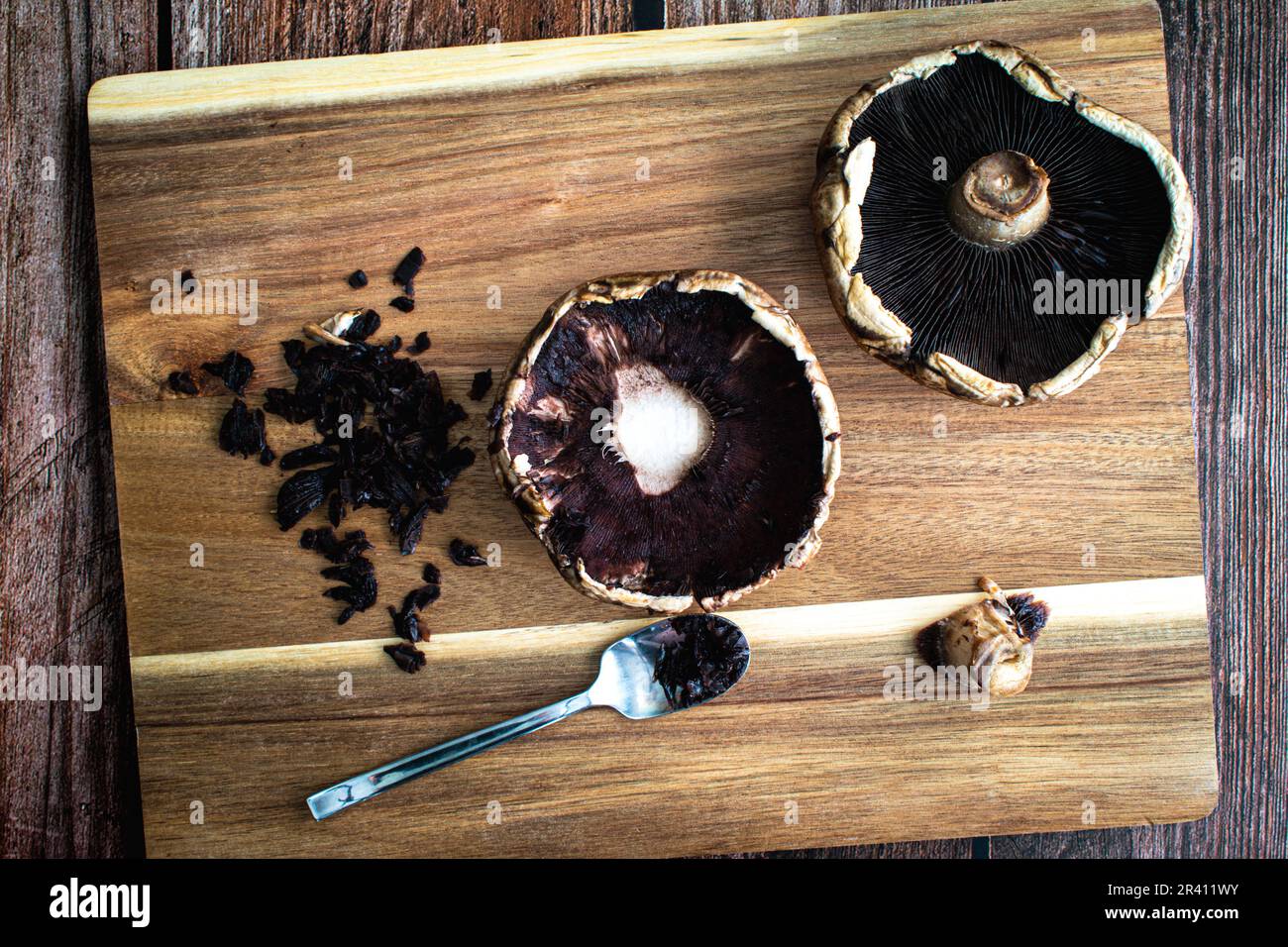 Nettoyage et endirage d'une paire de chapeaux de champignons Portobello : raclage des branchies des chapeaux de champignons crus sur une planche à découper en bois Banque D'Images