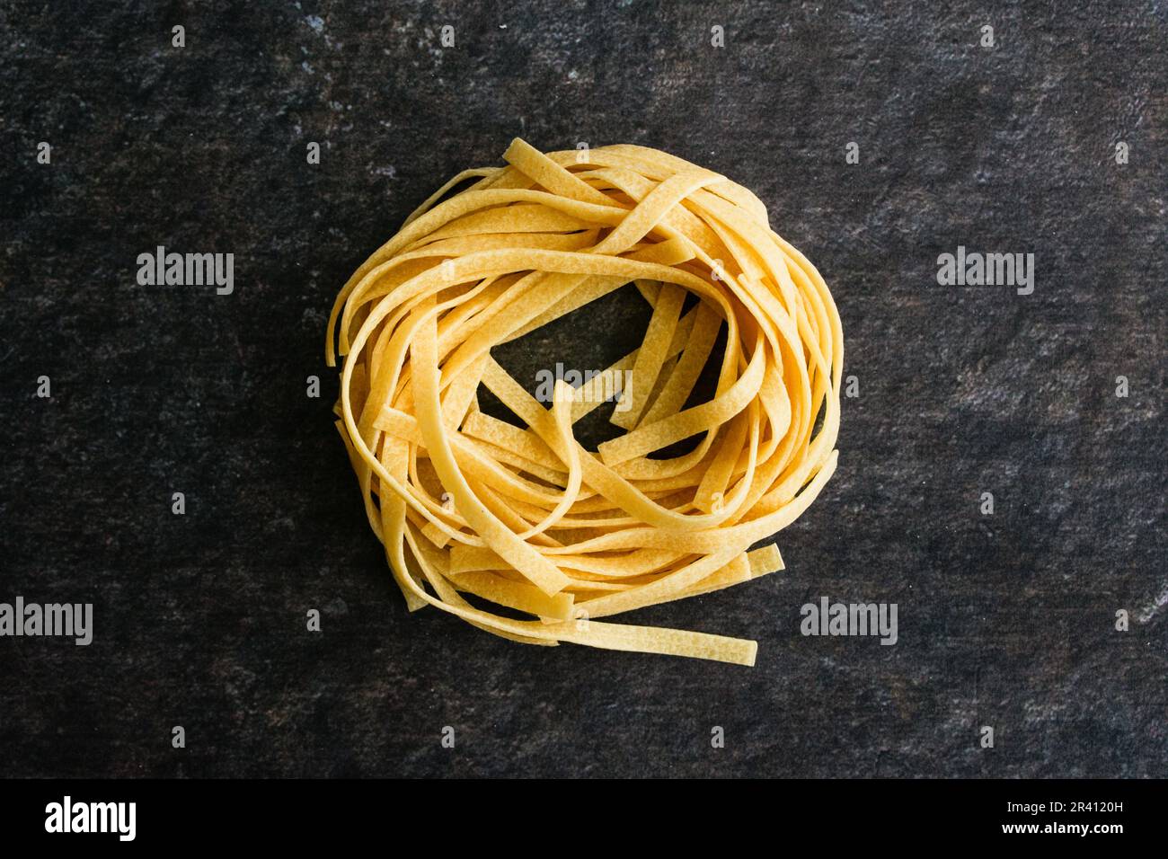Un seul Tagliatelle Pasta Nest sur un fond sombre : un nid de pâtes de nouilles séchées vu de près directement au-dessus Banque D'Images