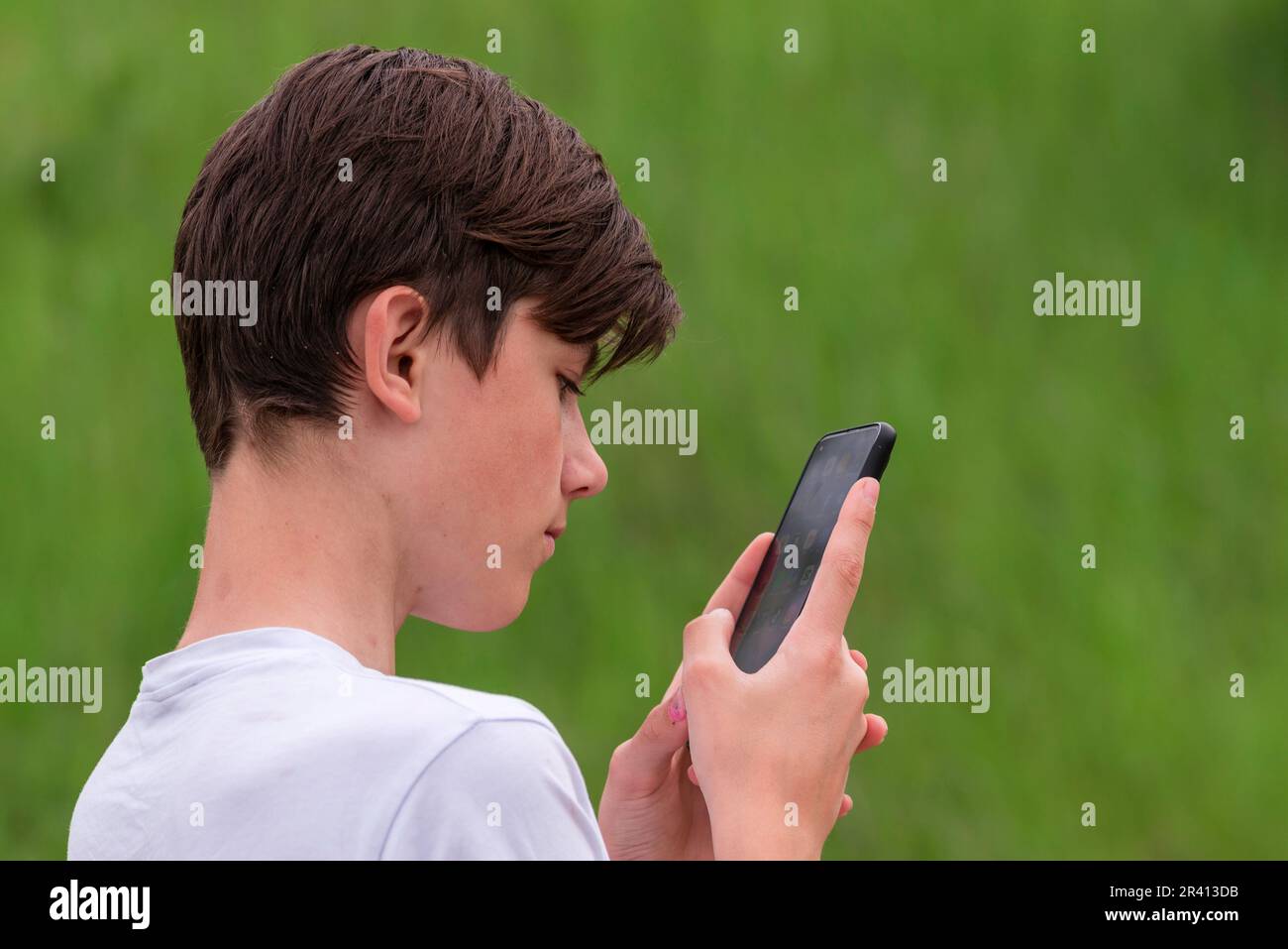 Adolescent regardant dans un téléphone intelligent à l'extérieur. Danger d'Internet vert nature de fond Banque D'Images