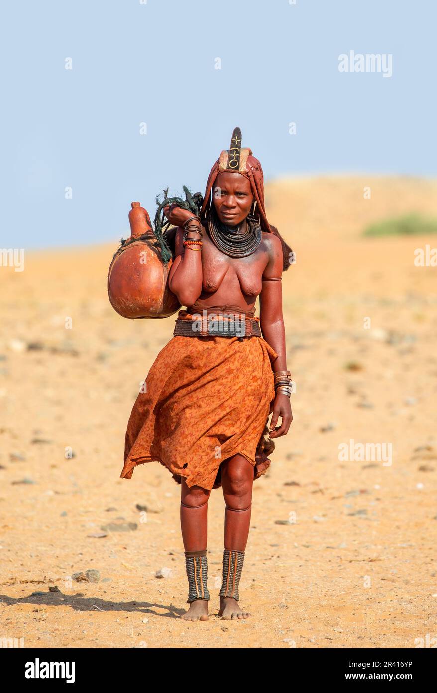La femme Himba marche dans le désert et porte un bateau d'eau Banque D'Images