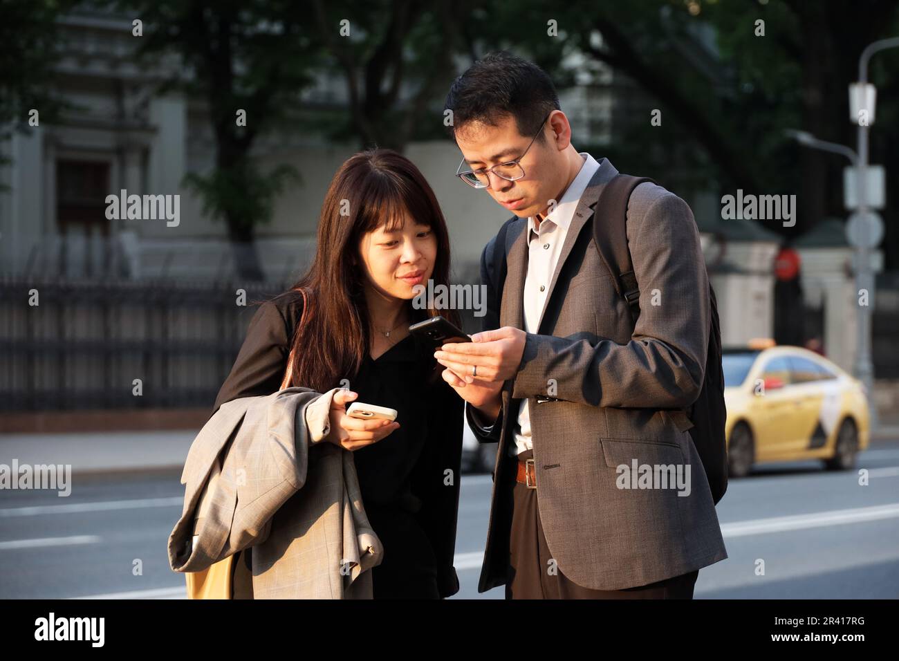 Couple asiatique debout avec des smartphones dans la rue de la ville sur fond de voiture de taxi Banque D'Images