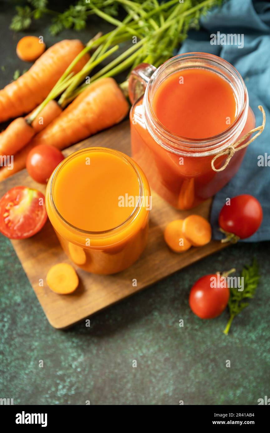 Jus de tomate et de carotte dans un verre et tomates fraîches sur un plan d'examen en pierre. Vitamines boissons jus carotte et tomate, Li sain Banque D'Images