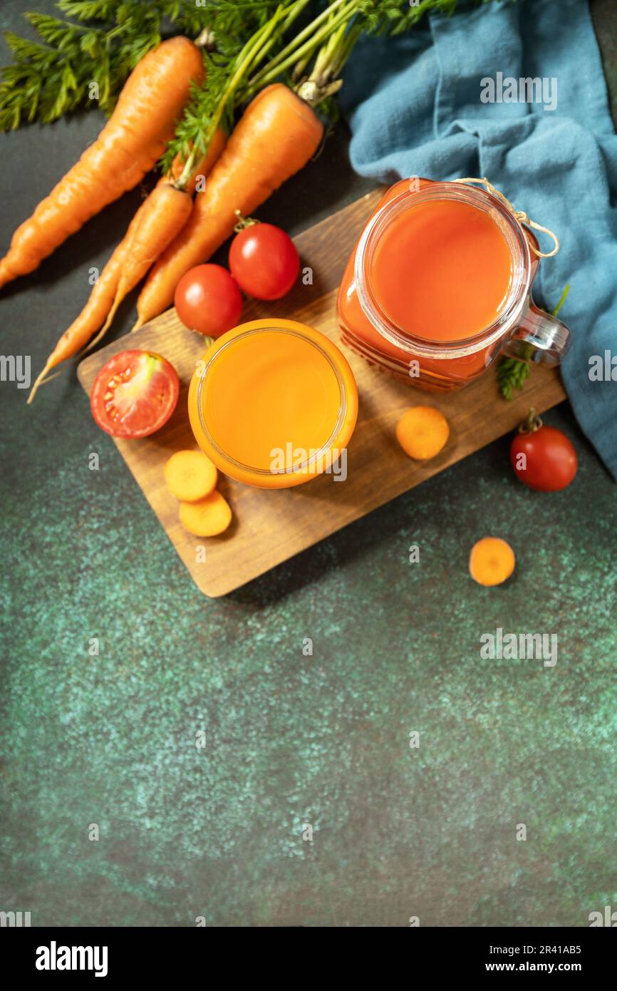 Vitamines boissons jus carotte et tomate, mode de vie sain. Jus de tomate et de carotte dans un verre et tomates fraîches sur une pierre t Banque D'Images