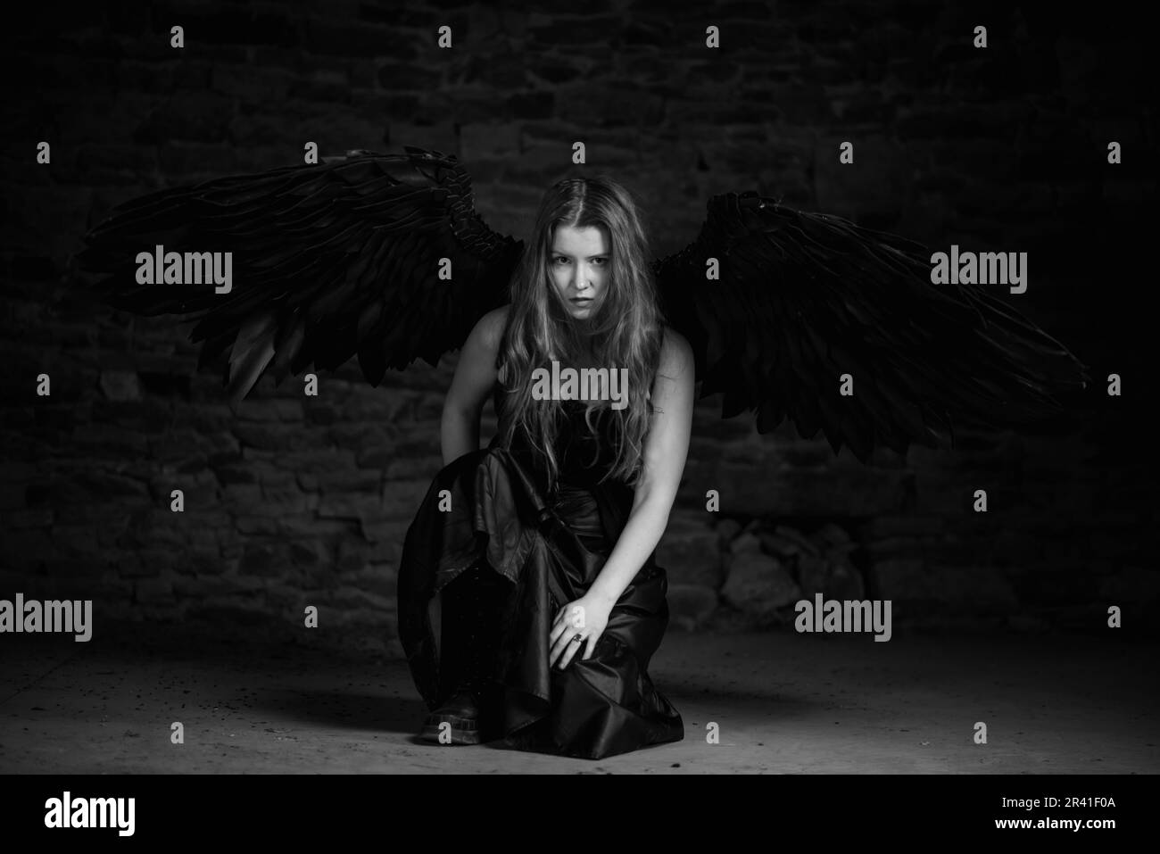 Ange noir aux cheveux rouges dans une pièce sombre. Arrière-plan en pierre sombre. Image en noir et blanc. Banque D'Images