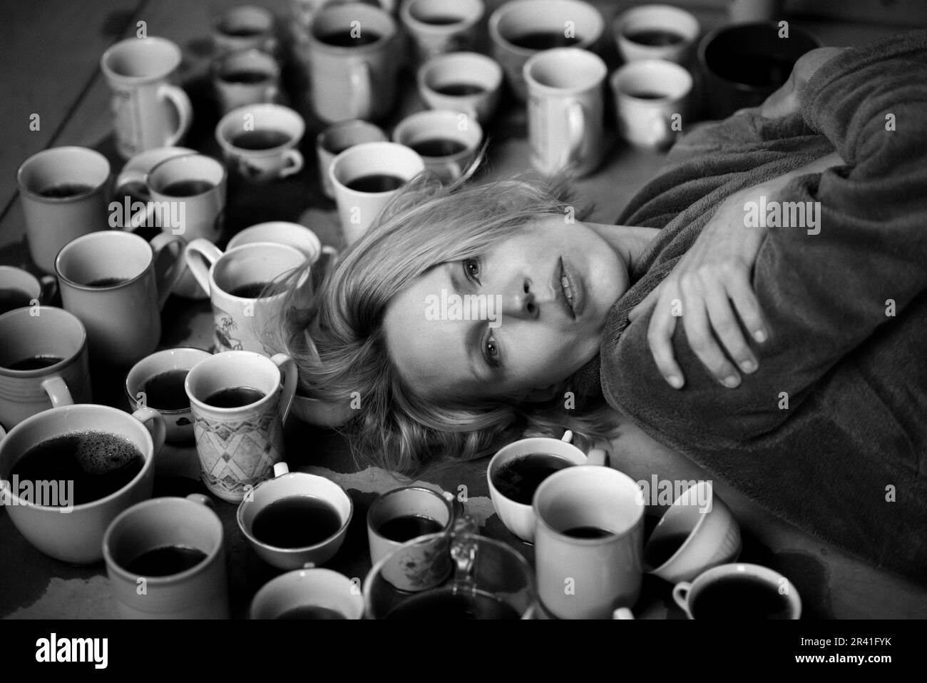 Femme entourée de nombreuses tasses de café, échéance concept. Le travail, les heures supplémentaires, la nécessité d'être alerte. Femme fatiguée. Photo en noir et blanc. Banque D'Images