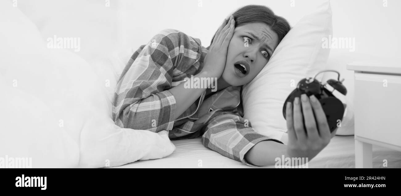 Jeune femme émotive avec réveil à la maison le matin. Photographie en noir et blanc Banque D'Images