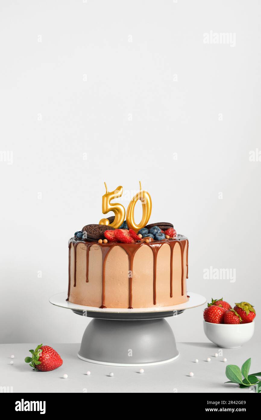 Gâteau d'anniversaire au chocolat avec baies, biscuits et bougies d'or numéro cinquante sur fond blanc, espace de copie Banque D'Images