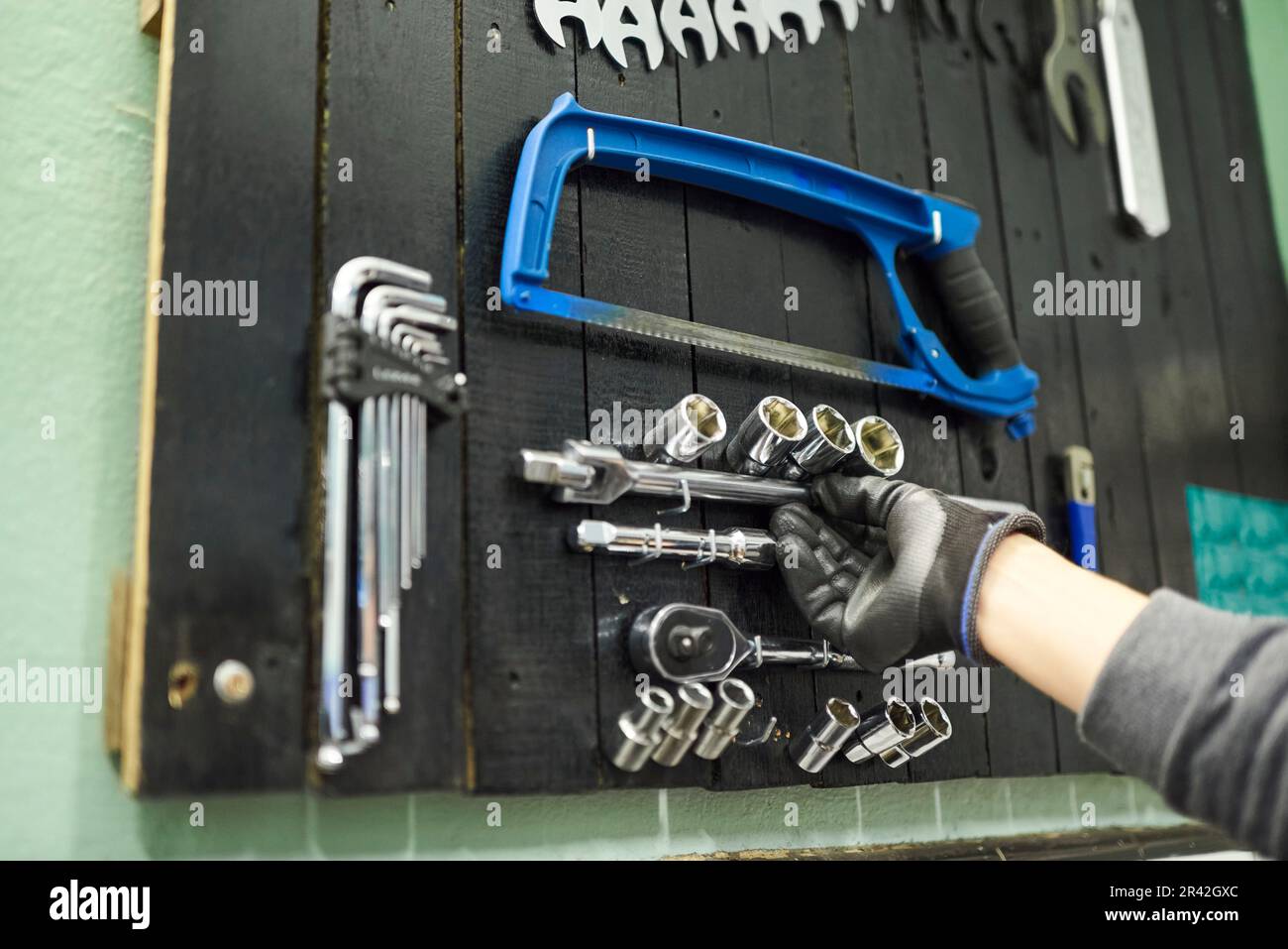 Main d'une personne non reconnaissable portant un gant de protection saisissant un article sur une planche à outils dans le mur d'un atelier de réparation de vélo. Banque D'Images