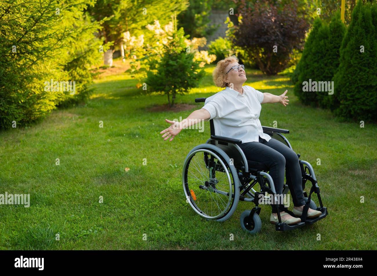 Une vieille femme heureuse a étendu ses bras sur les côtés tout en étant assise dans un fauteuil roulant sur une promenade à l'extérieur. Banque D'Images