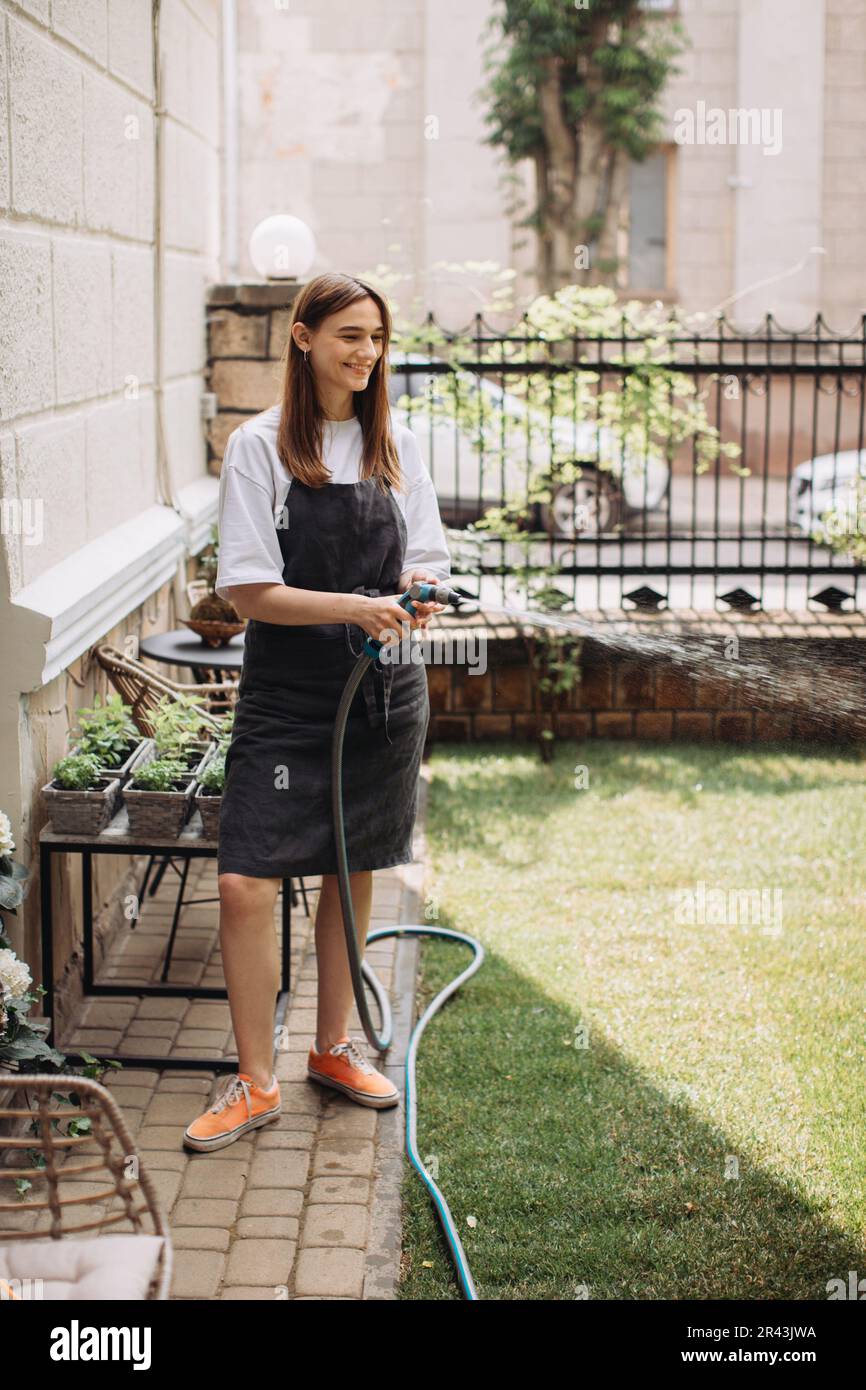 Femme arroser des herbes fraîches poussant à la maison jardin potager. Jardinier prenant soin des plantes à l'arrière-cour de sa maison. Concept de durabilité an Banque D'Images