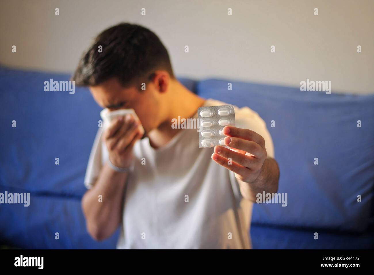 Homme froid assis sur le canapé avec un mouchoir et des médicaments. Banque D'Images Homme froid assis sur le canapé avec un mouchoir et des médicaments. Banque D'Images