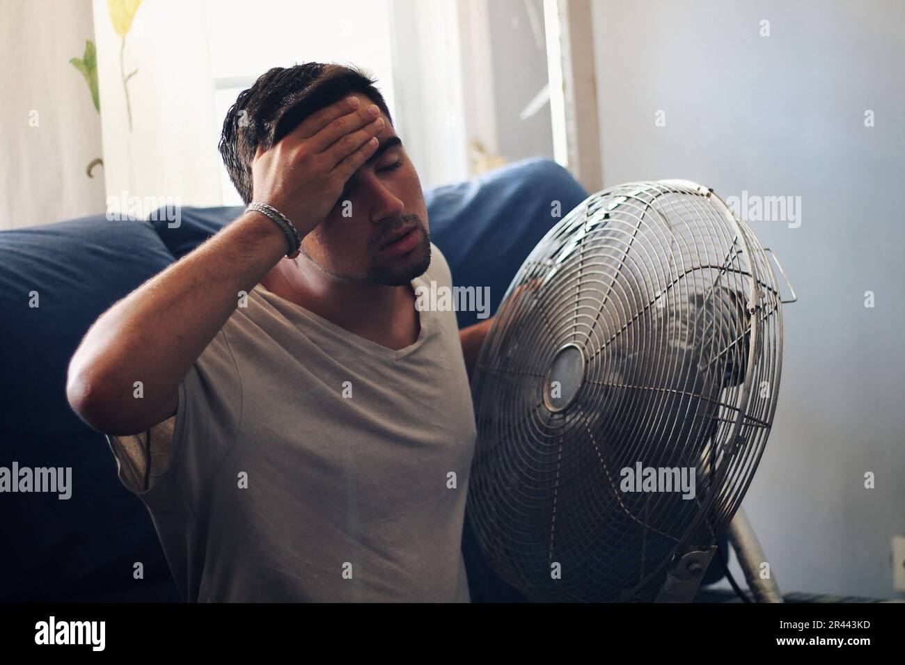 Homme habillé de blanc avec la chaleur et un ventilateur à côté. Banque D'Images