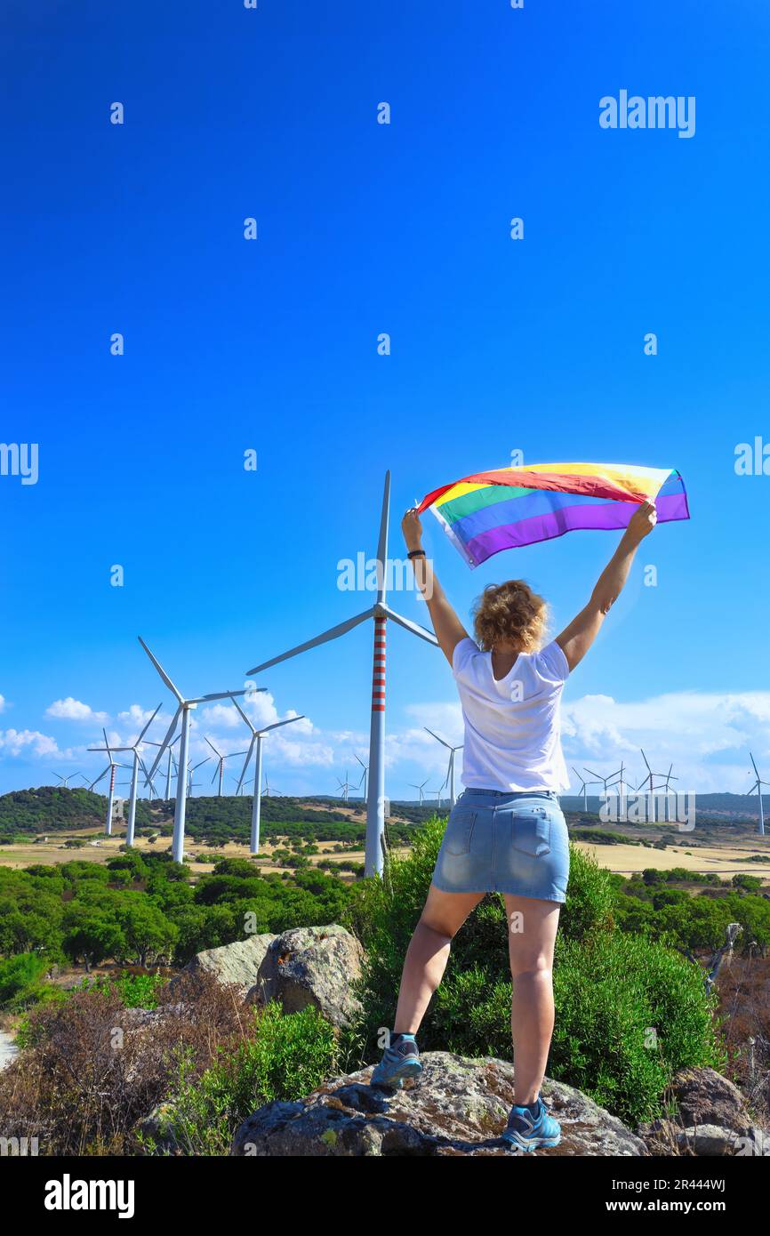 femme levant un drapeau arc-en-ciel devant des éoliennes. Banque D'Images