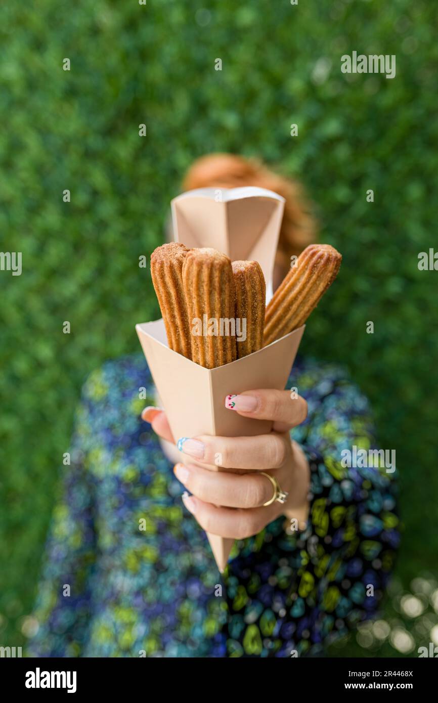 femme tenant des churros dans une boîte en carton devant le mur d'herbe verte Banque D'Images